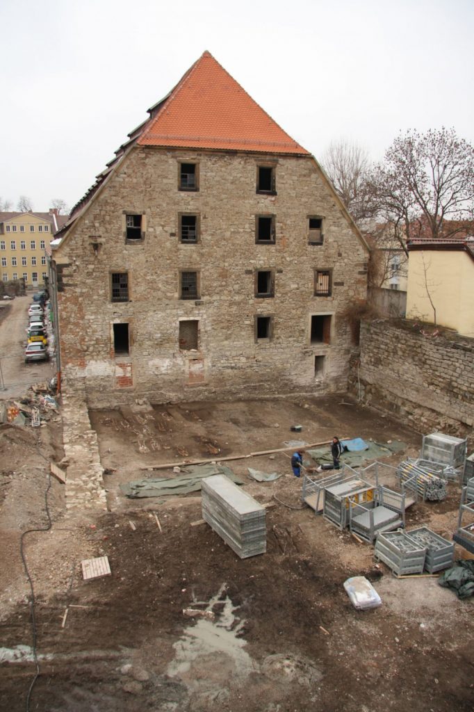 15. yüzyıldan kalma tahıl ambarı (büyük kahverengi bina) Almanya'nın Erfurt kentinde bir otoparka dönüştürülürken, altındaki Yahudi mezarlığından mezarlar ortaya çıkarıldı. Kalıntıları yakındaki 19. yüzyıldan kalma bir Yahudi mezarlığına taşımak için yapılan bir kurtarma kazısından sonra, bir erişim rampası yerleştirildi (bu resimde sağda dairesel yapı). Kredi: Shai Carmi, Kudüs İbrani Üniversitesi